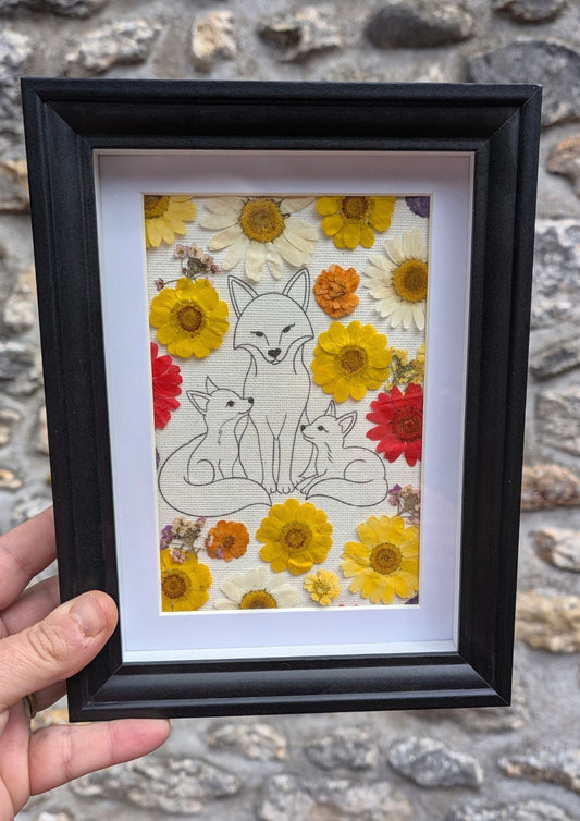 Cadre fleuri Famille Renard tenu en main pour visualiser son format, avec illustration et véritables fleurs pressées.