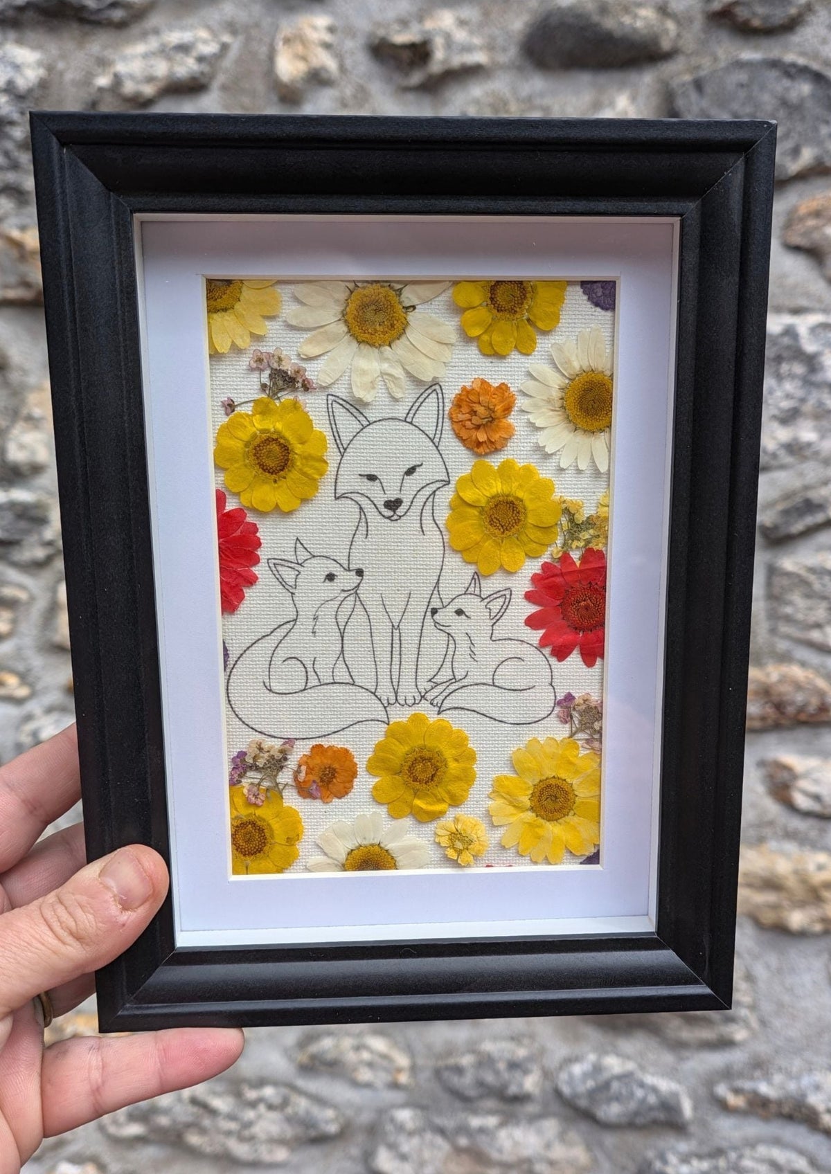 Cadre fleuri Famille Renard tenu en main pour visualiser son format, avec illustration et véritables fleurs pressées.
