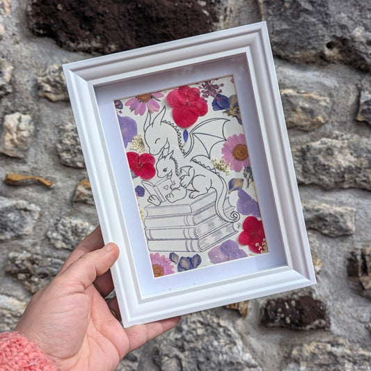 Cadre fleuri Histoire du soir tenu en main pour visualiser son format, avec deux dragons et de véritables fleurs séchées sous presse.