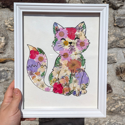 Cadre Néo tenu en main pour visualiser son format, représentant un chat fleuri réalisé à partir de véritables fleurs séchées et pressées.