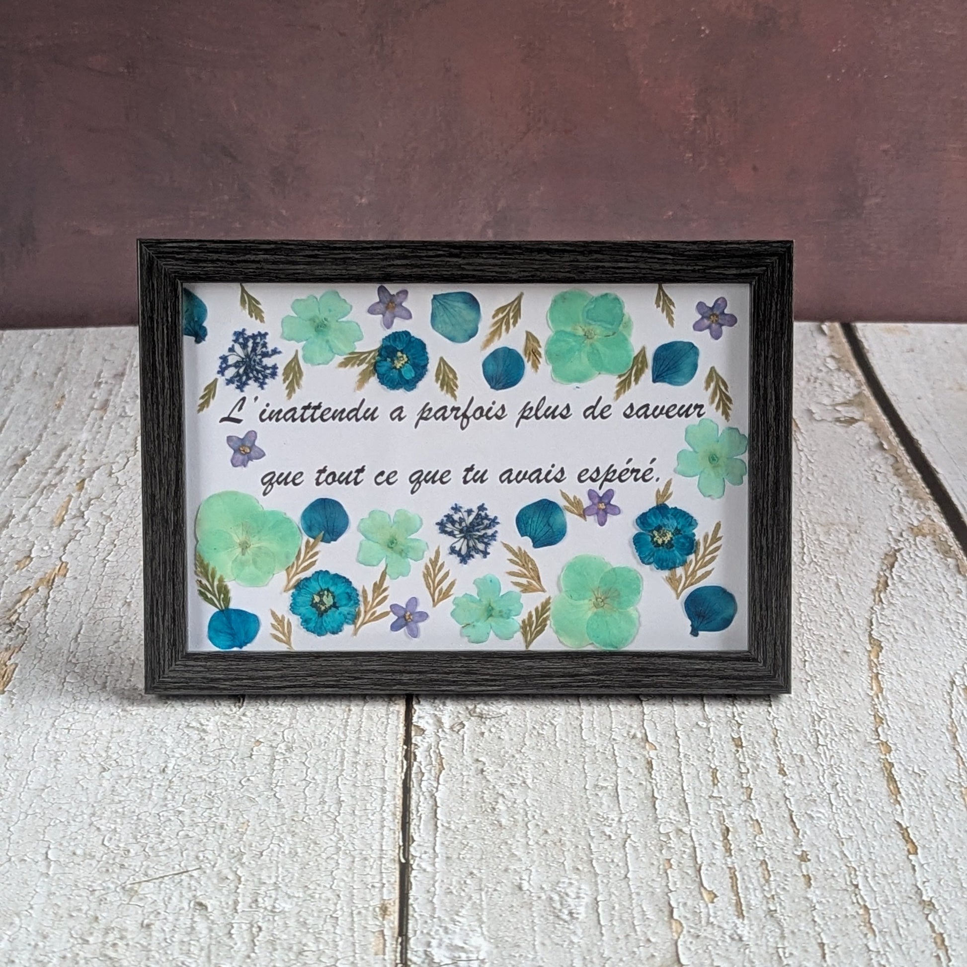 Cadre avec message « L’inattendu a parfois plus de saveur que tout ce que tu avais espéré », décoré de fleurs séchées bleues et turquoise, collection Florésie