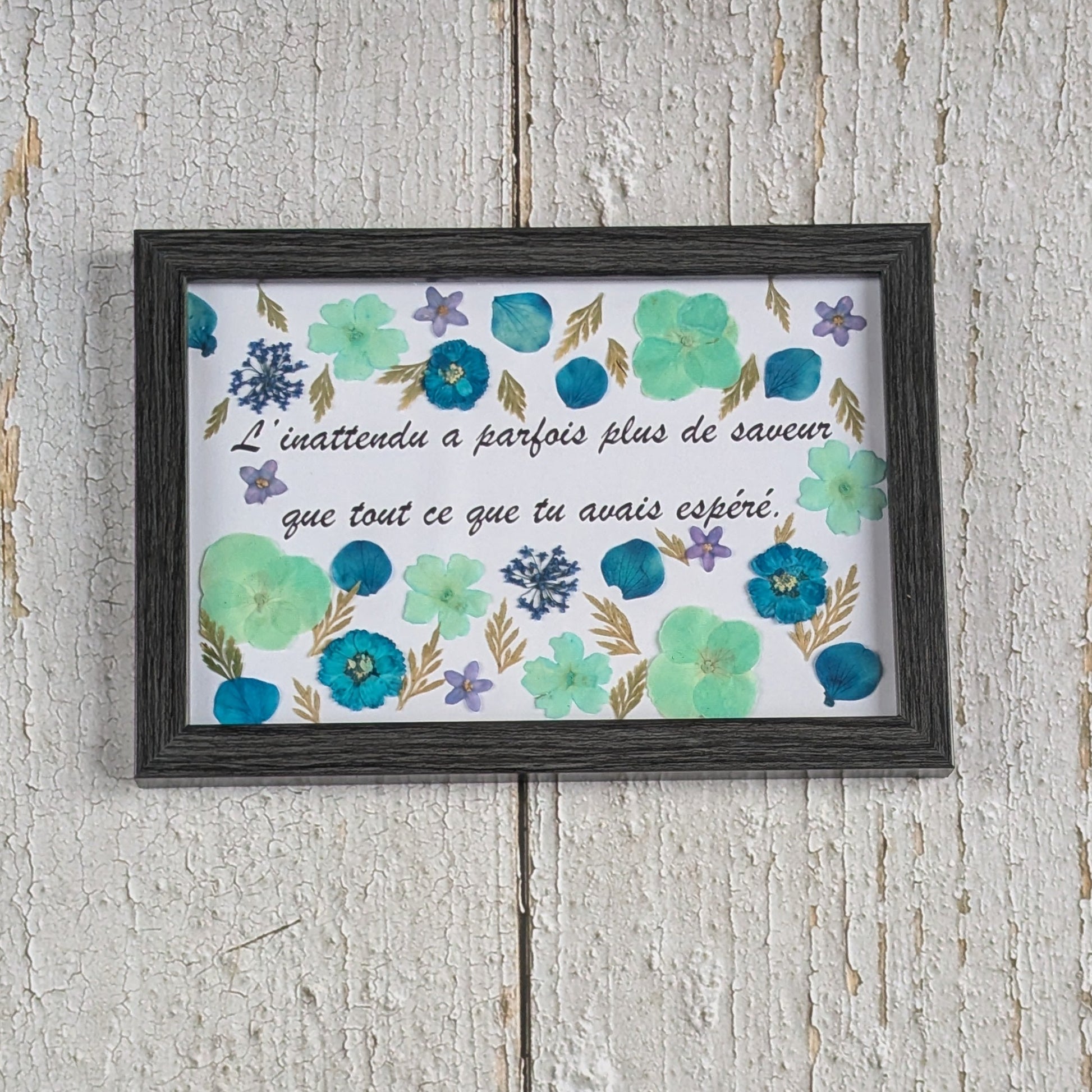Cadre avec message « L’inattendu a parfois plus de saveur que tout ce que tu avais espéré », décoré de fleurs séchées bleues et vertes, collection Florésie