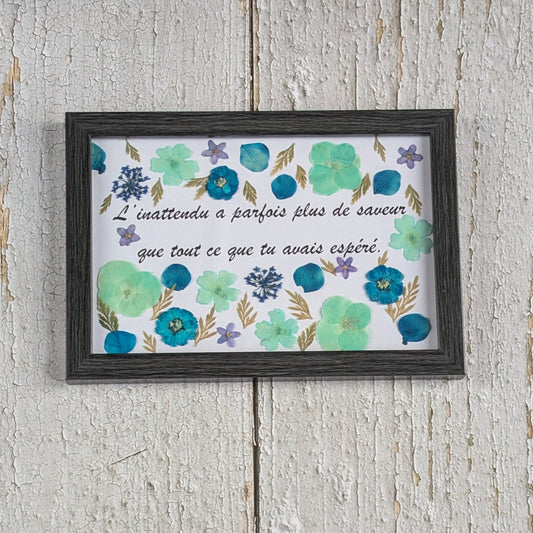 Cadre avec message « L’inattendu a parfois plus de saveur que tout ce que tu avais espéré », décoré de fleurs séchées bleues et vertes, collection Florésie