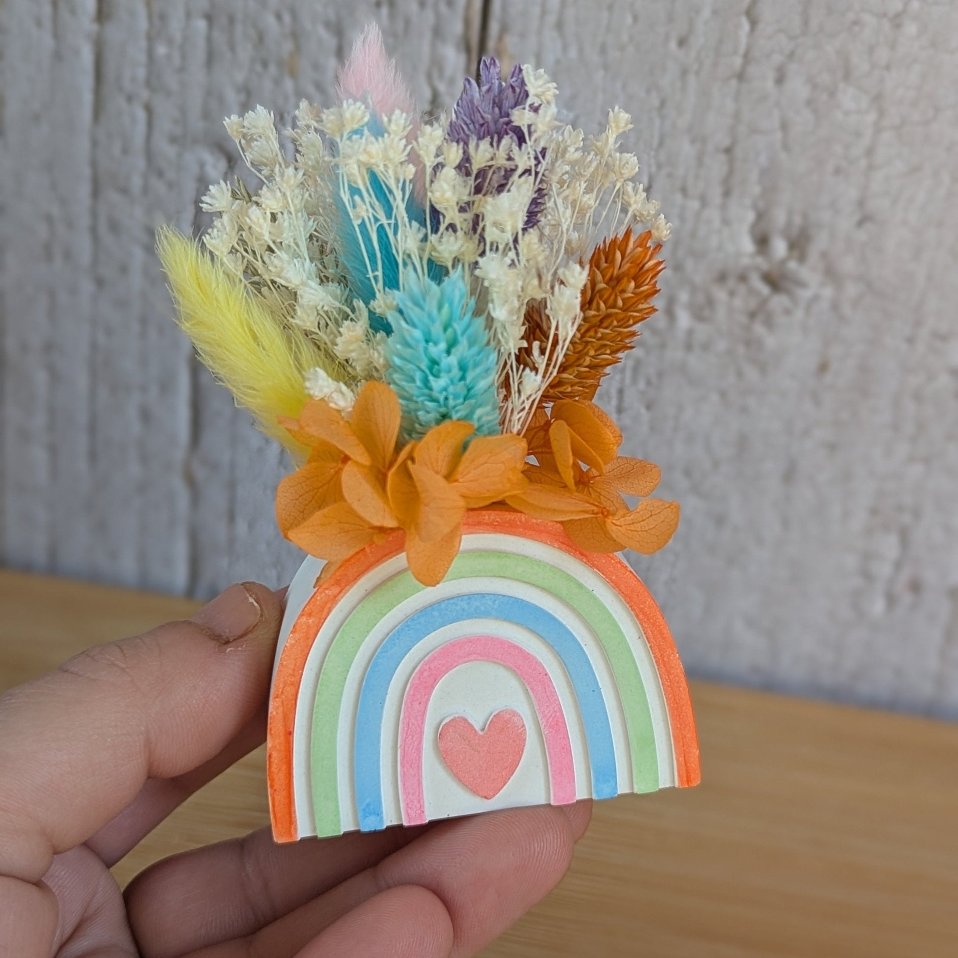 Bouquet de fleurs séchées dans un petit vase arche en résine minérale tenu à la main, collection Sorane